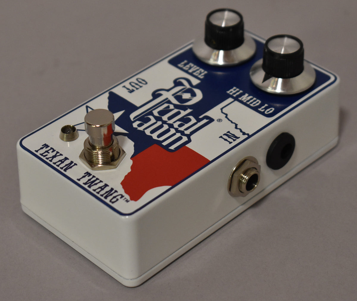 The white pedal, angled from the front right, features a Texas flag graphic, two silver-capped black knobs, and a chrome footswitch.