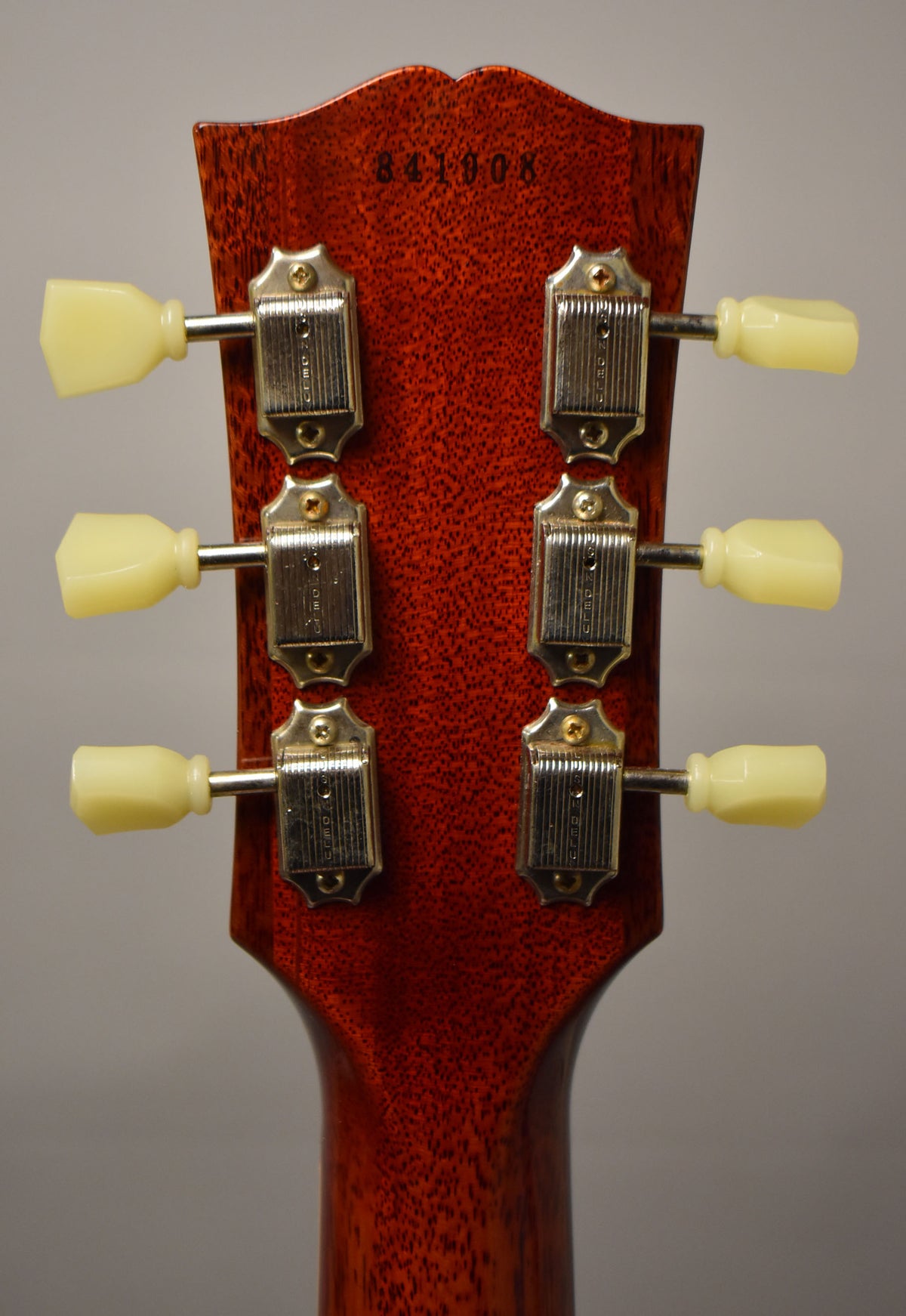 Rear view of the headstock and upper neck, showing the dark red wood grain, six aged nickel tuners, and cream buttons.