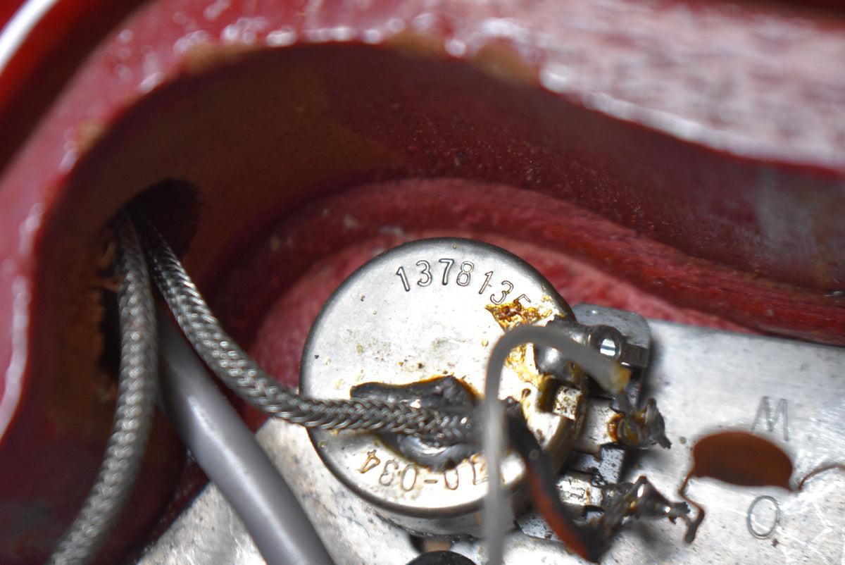 Close-up of the guitar's wiring cavity, showing a tarnished pot with visible numbers and braided wires.