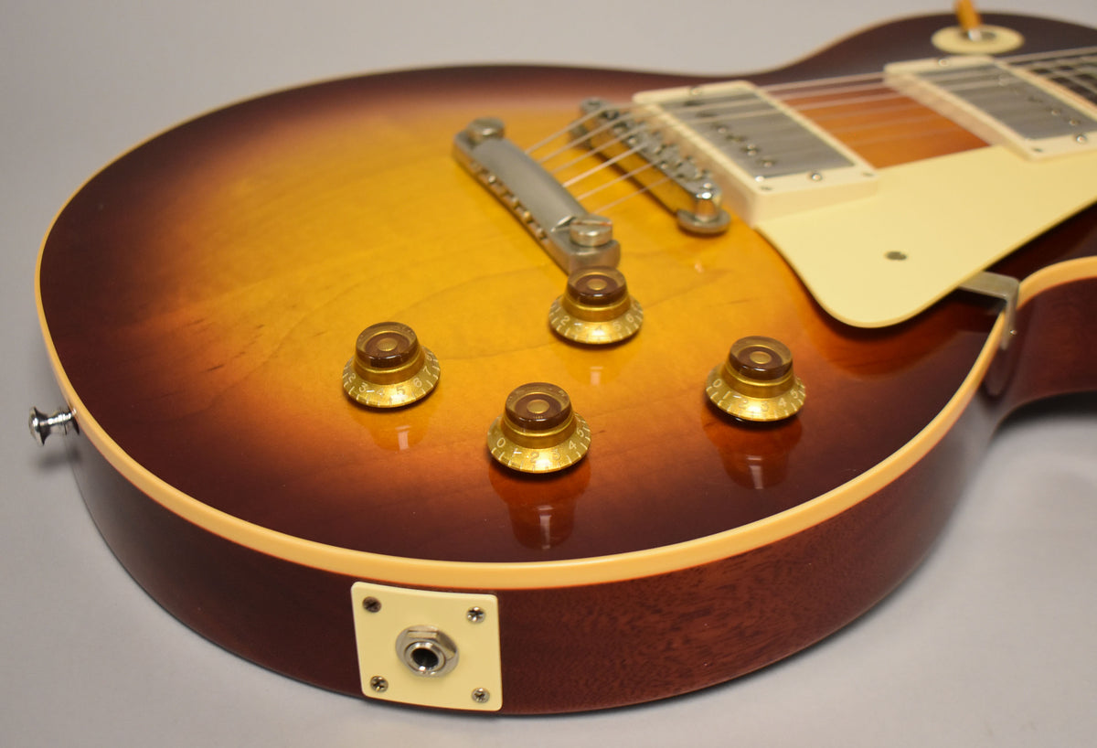 The guitar's lower bout, showing the Bourbon Burst finish, four amber top hat knobs, cream pickguard, and output jack.