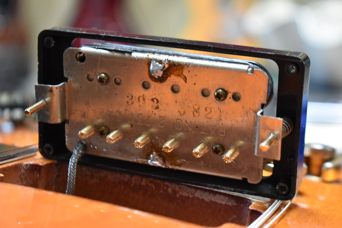 Close-up of the pickup's underside, revealing a silver baseplate with gold pole pieces, visible wiring, and some solder residue.