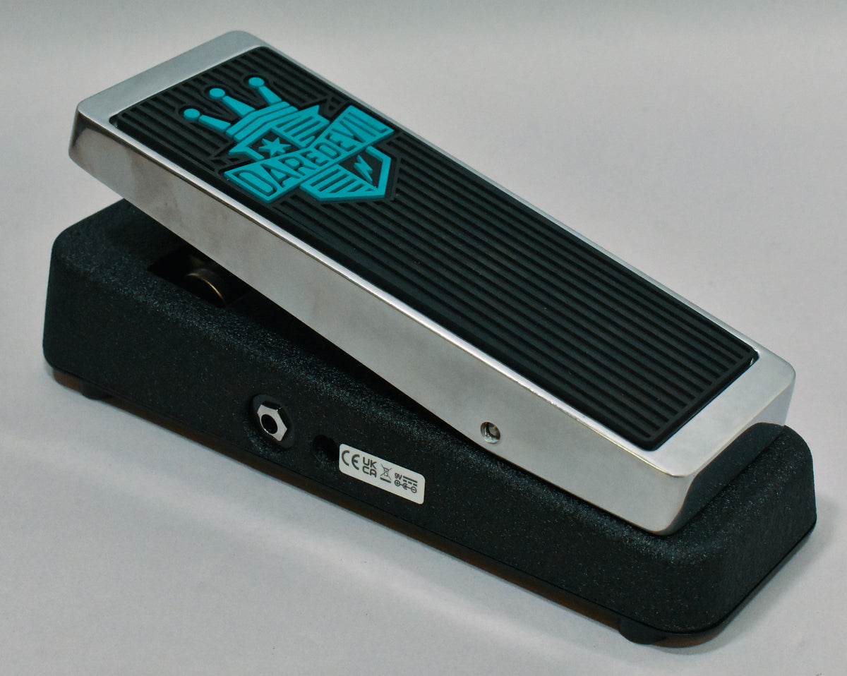 The black textured pedal base and chrome rocker are angled, revealing a black rubber tread with a teal crown and shield logo.