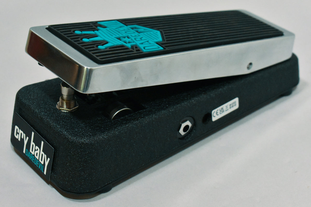 The black textured wah pedal is angled right, showing its brushed metal rocker with a black rubber tread and teal graphic.