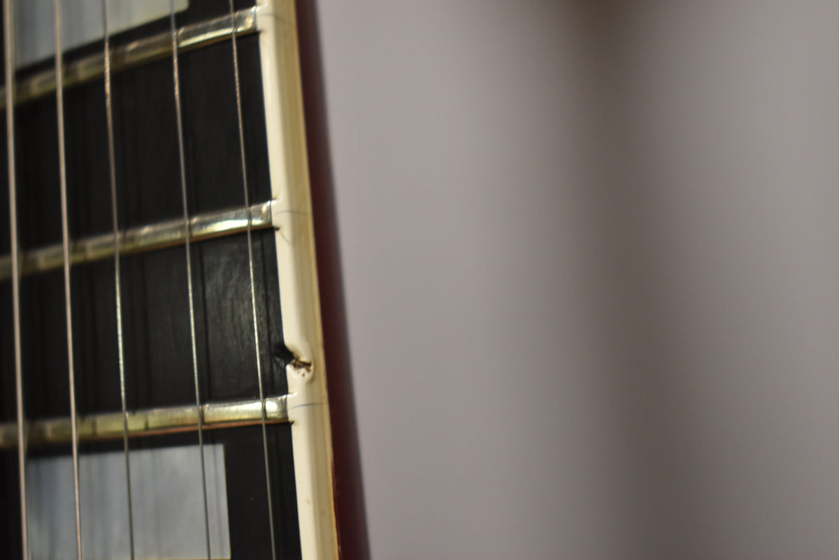 Close-up of the fretboard and binding, showing a chip in the cream binding near the 1st fret and light wear on the frets.