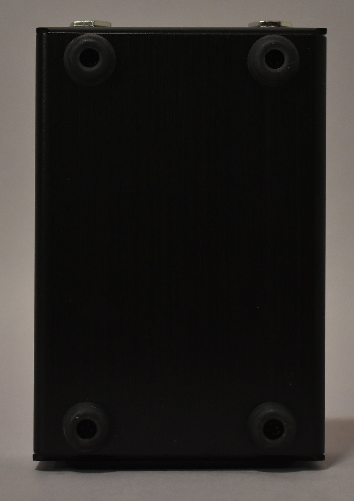 The bottom of the black metal pedal is visible, showing four round black rubber feet and a slight scuff on the lower right foot.