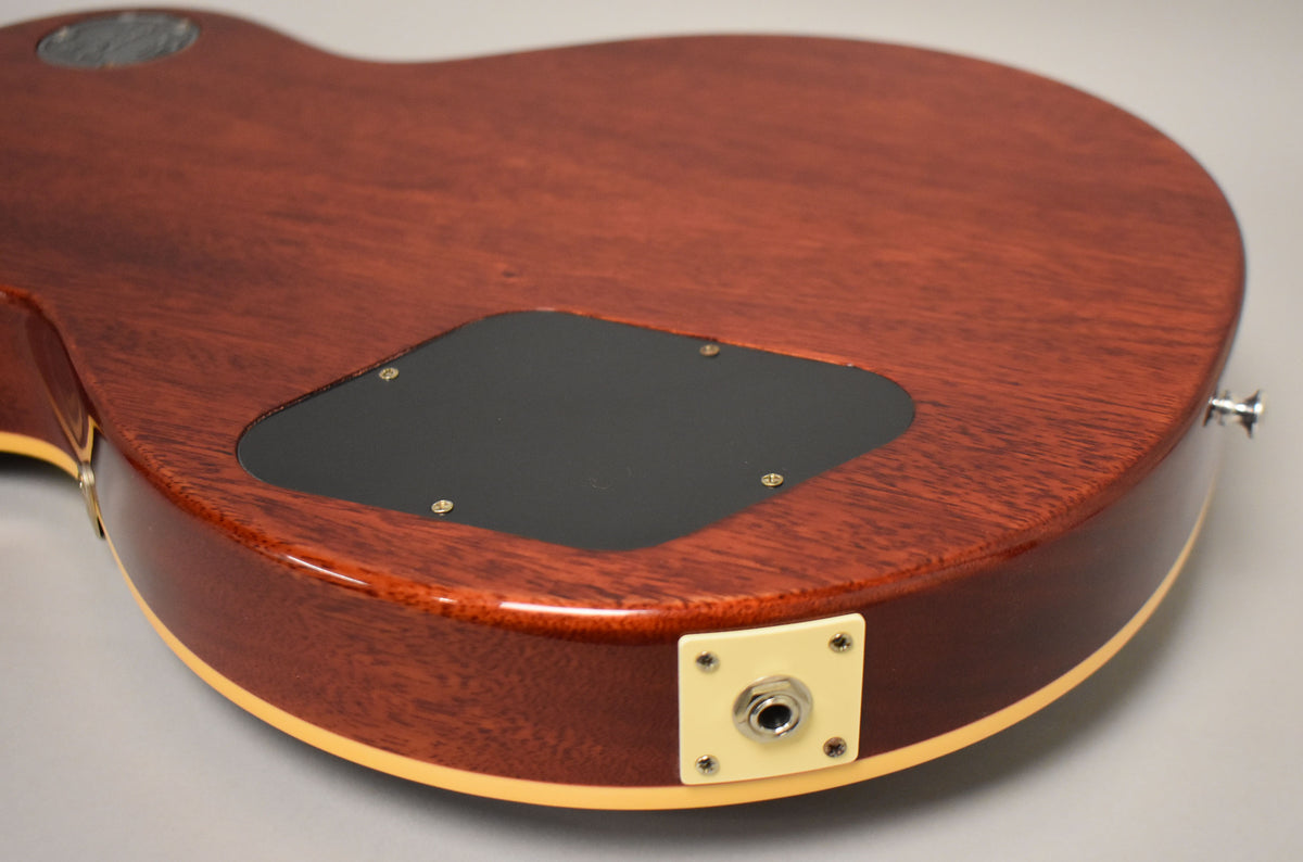 The guitar's mahogany back and side, with a black control cavity cover and cream output jack plate, are shown from a low angle.