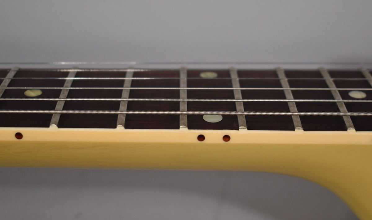 Close-up of the dark fretboard with light fret markers and strings, showing the light-yellow neck with two small side dots.