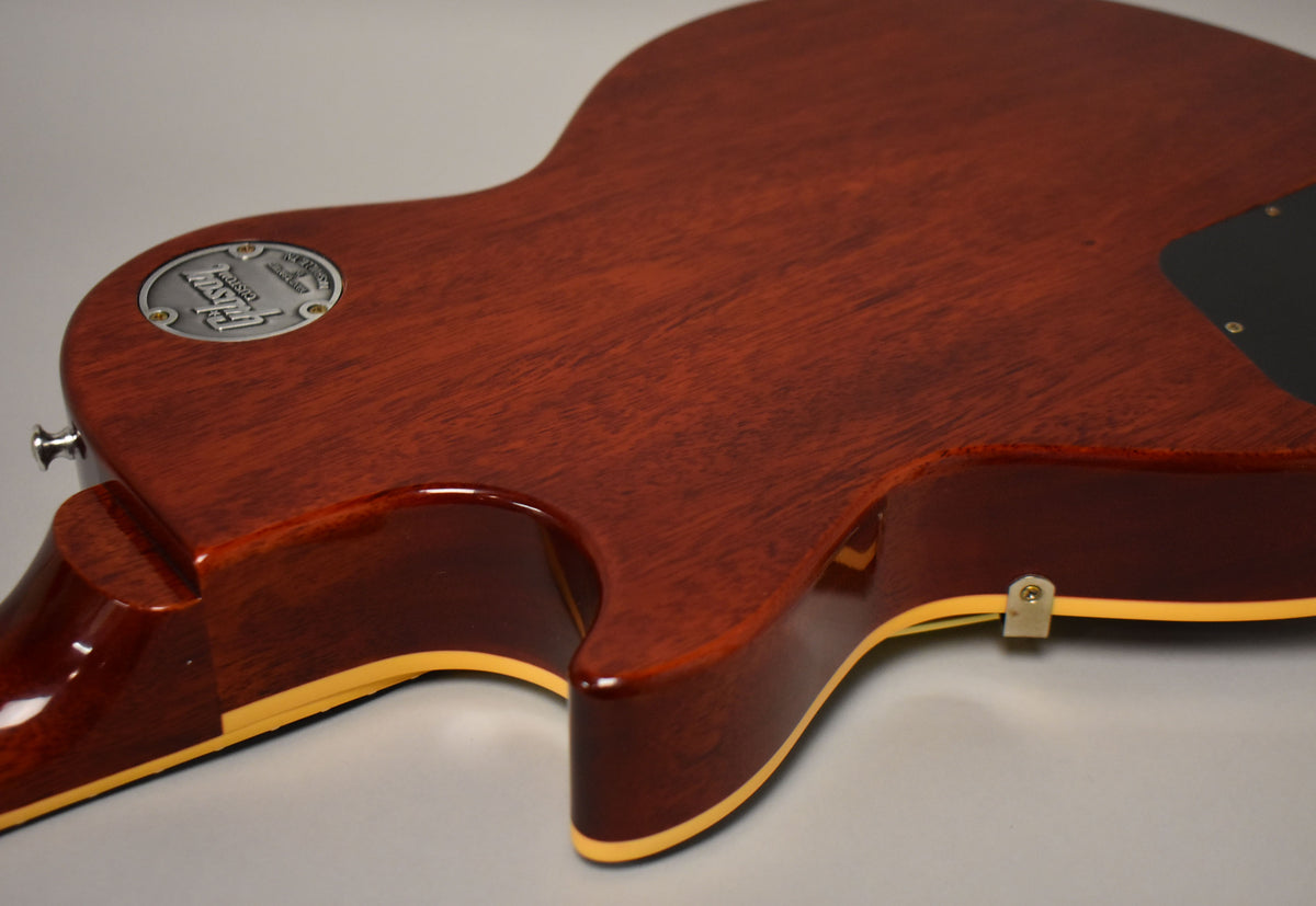 The guitar's dark reddish-brown back shows wood grain, with a metal medallion near the neck and a cream binding along the edges.
