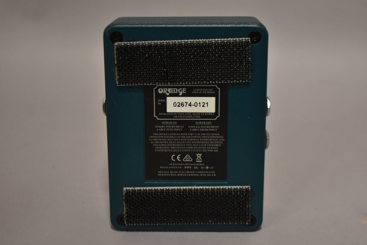 The teal pedal is viewed from the back, showing two strips of black hook-and-loop tape and a data label.