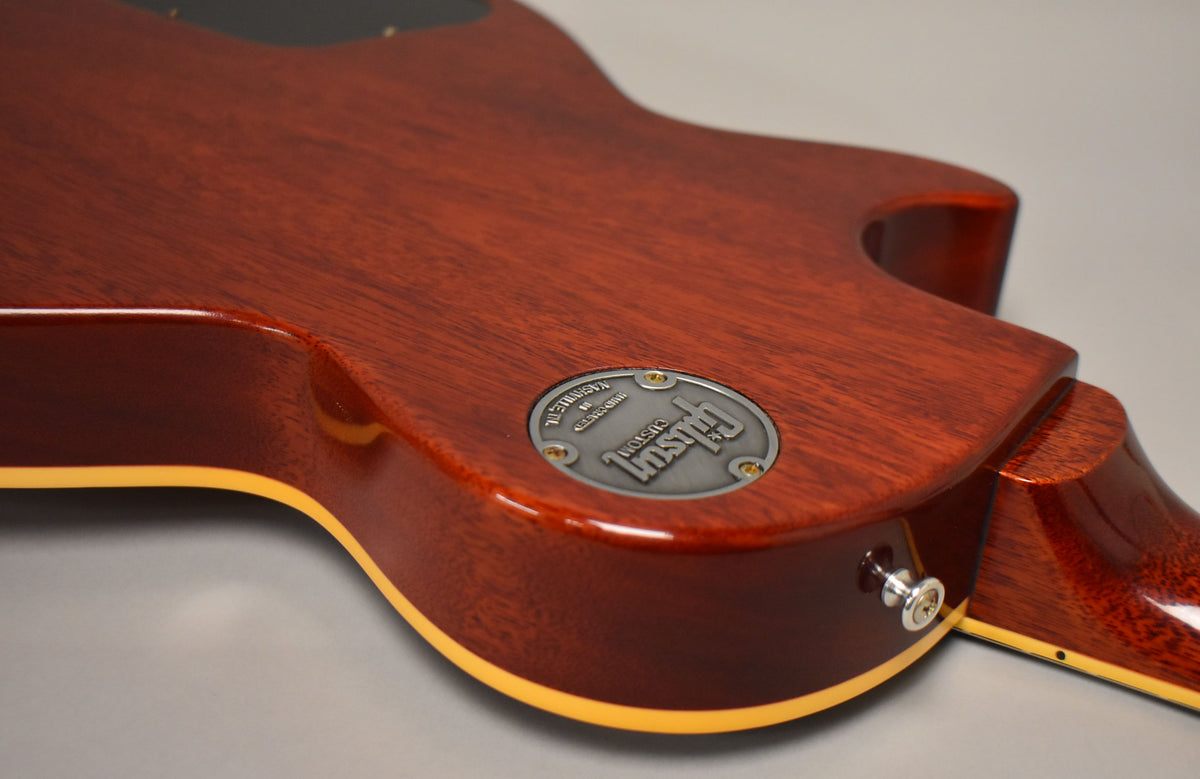The guitar's mahogany back and neck heel are visible, with a silver-colored medallion and a chrome strap button on the lower bout.