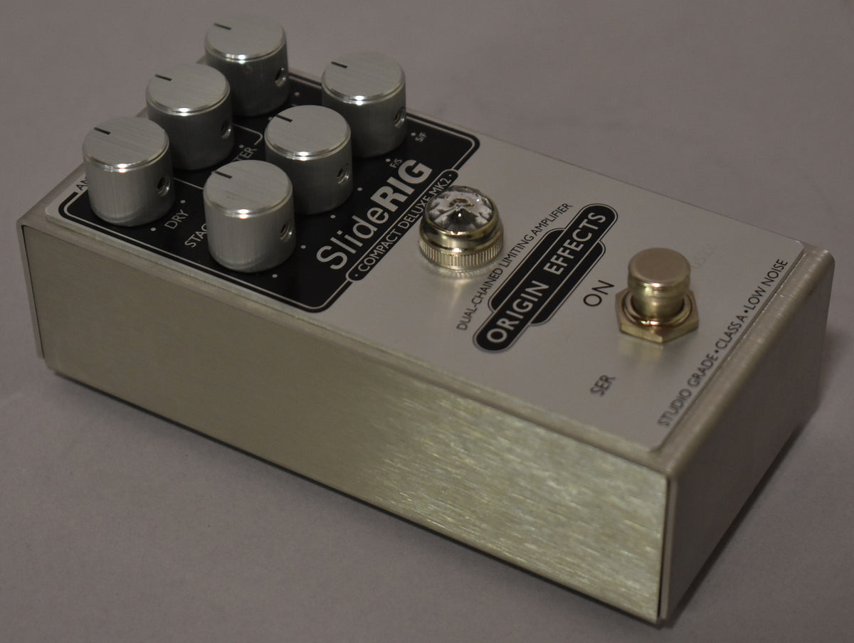 Brushed silver pedal with six silver knobs, a clear jewel lamp, and a gold footswitch, viewed from the top right.