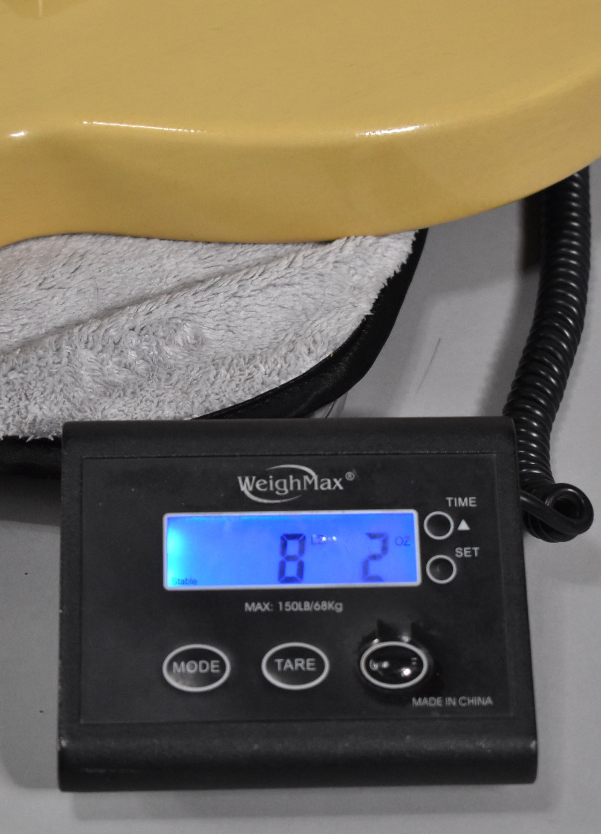 The TV yellow guitar body rests on a soft case lining, with a digital scale displaying "8 Lb 2 Oz" below.