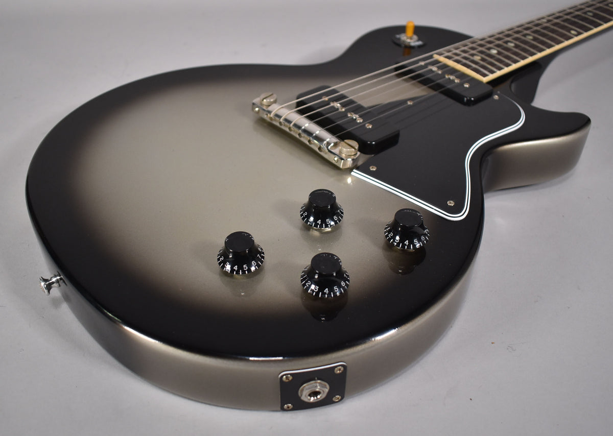 The guitar's body, angled from above, shows a silverburst finish, black pickguard, four black control knobs, and a P90 pickup.
