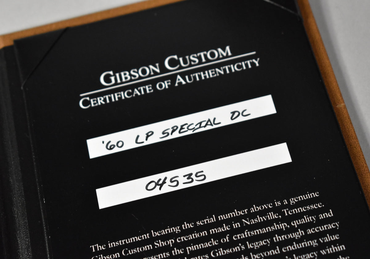 Close-up of a black "Gibson Custom Certificate of Authenticity" with handwritten " '60 LP SPECIAL DC" and "04535" on white labels.