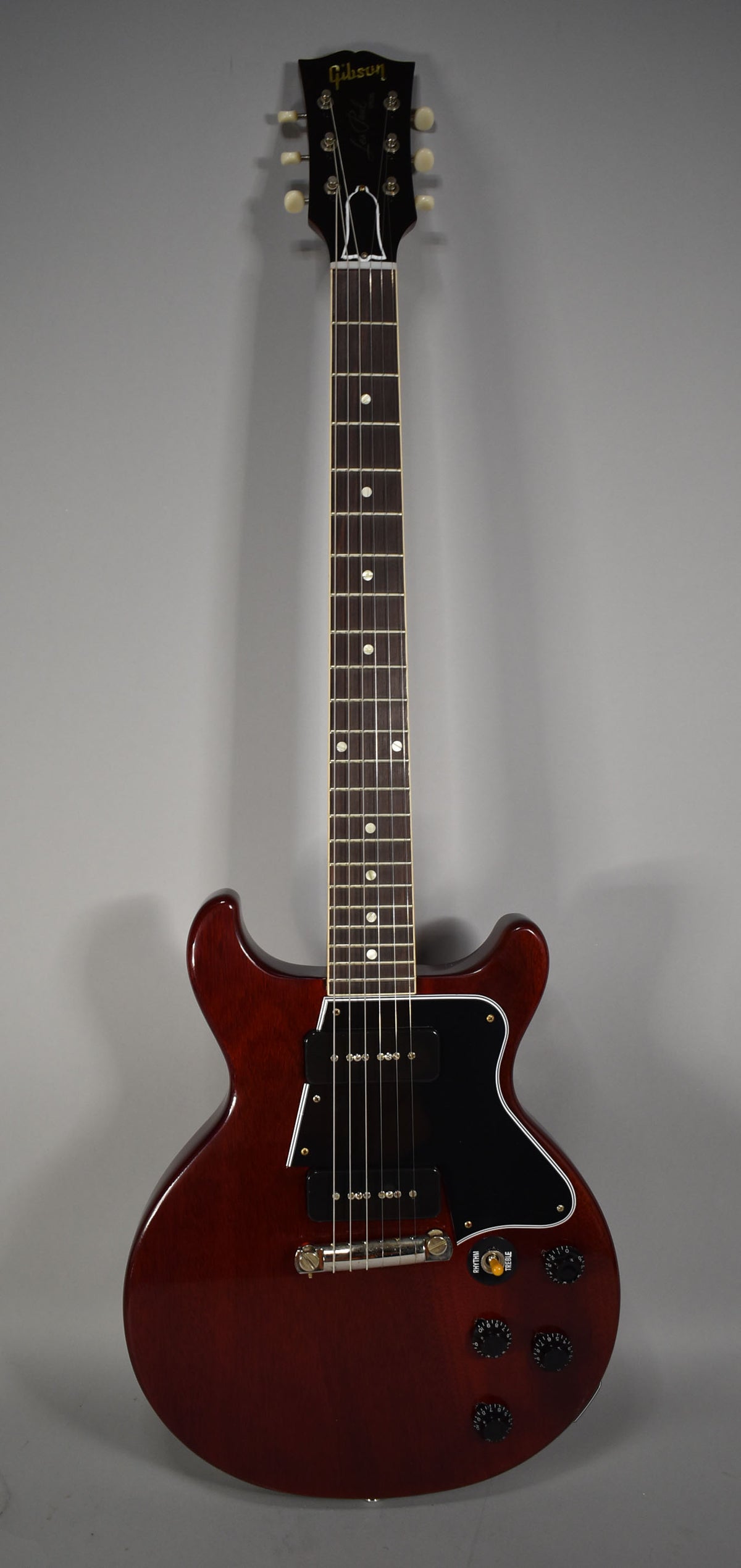 Full-length view of a cherry red double-cutaway electric guitar with a black pickguard, two P90 pickups, and four black control knobs.