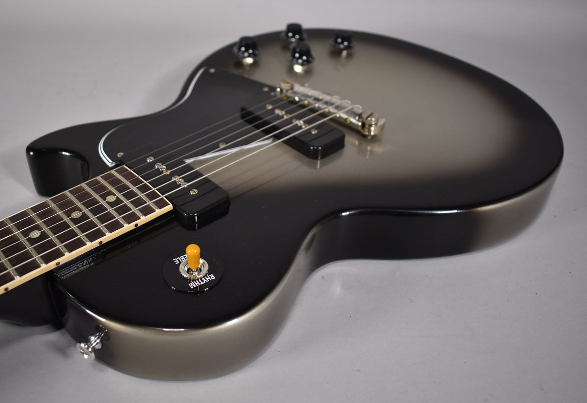 The guitar's body, in a silverburst finish, is angled from the lower bout, showing two P90 pickups and an amber switch tip.