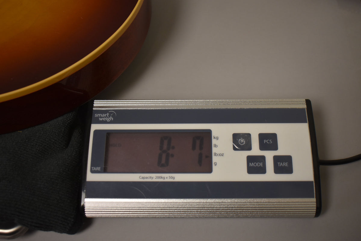 The guitar's Bourbon Burst body is partially visible, resting on a black cloth, next to a digital scale displaying "8 lb: 1 oz".