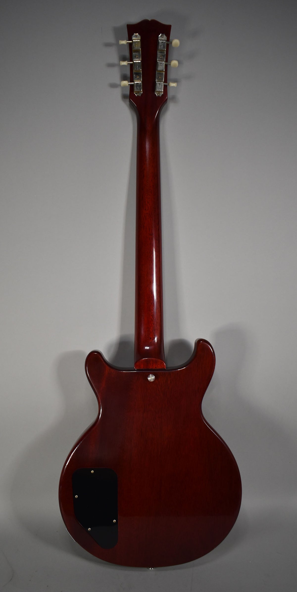 The cherry red guitar's back is visible, showing the neck, headstock with six cream tuners, and a black control cavity cover.