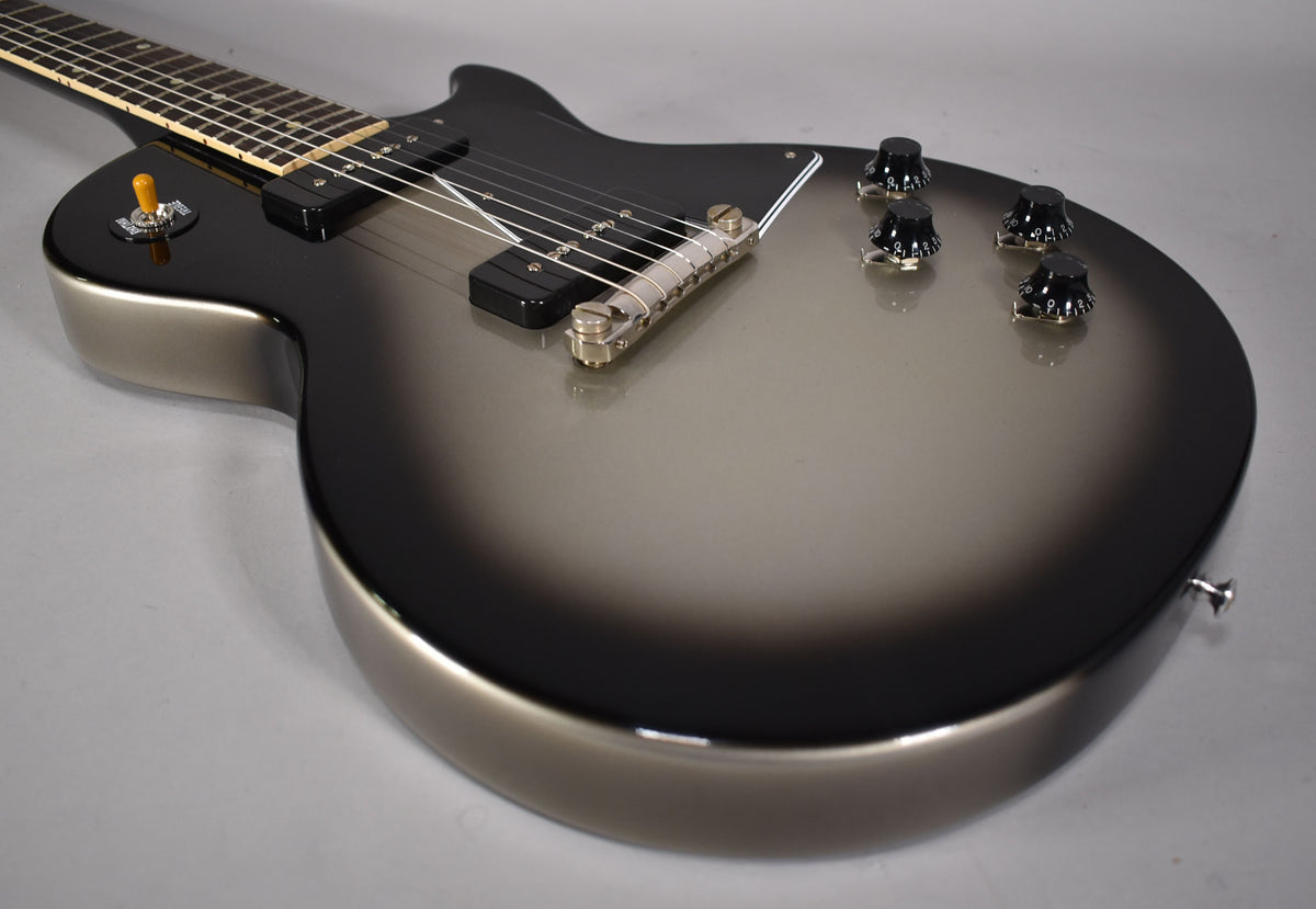 The guitar's body, angled from the neck, shows a silverburst finish with two P-90 pickups, a tune-o-matic bridge, and four black control knobs.