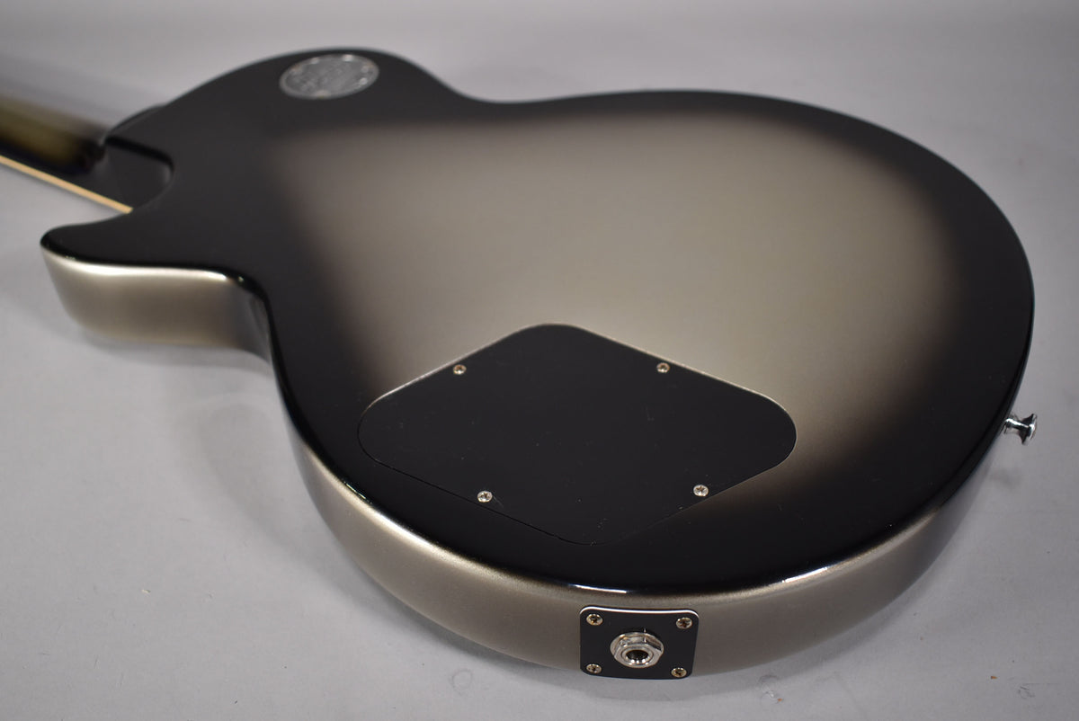 The guitar's back, angled from the neck, shows a silverburst finish, black control plate, and chrome output jack.