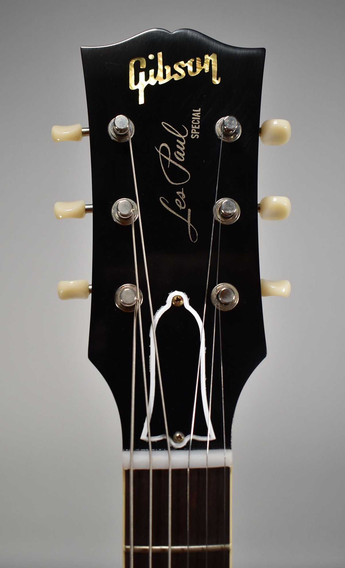 Close-up of the black headstock, showing six cream tuning pegs, a bell-shaped truss rod cover, and the top of the fretboard.