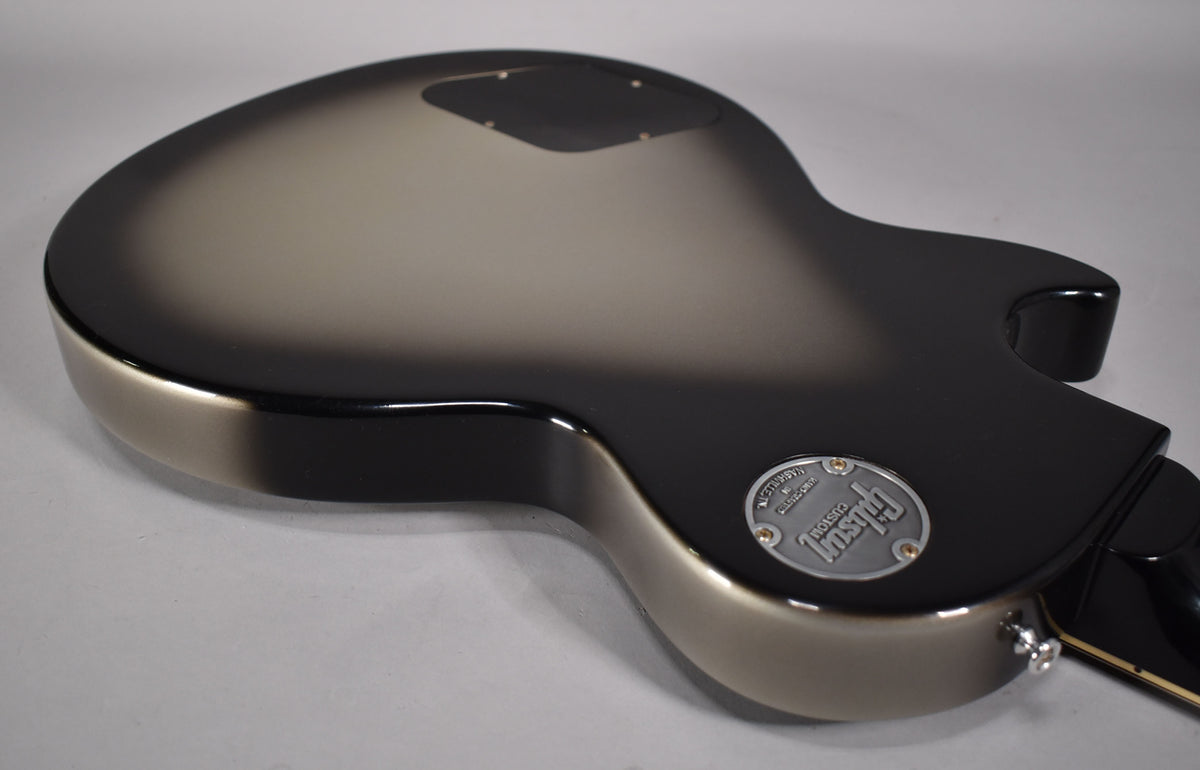 The guitar's back, angled from the lower bout, shows a silverburst finish, black control cavity cover, and a silver "Custom" medallion.
