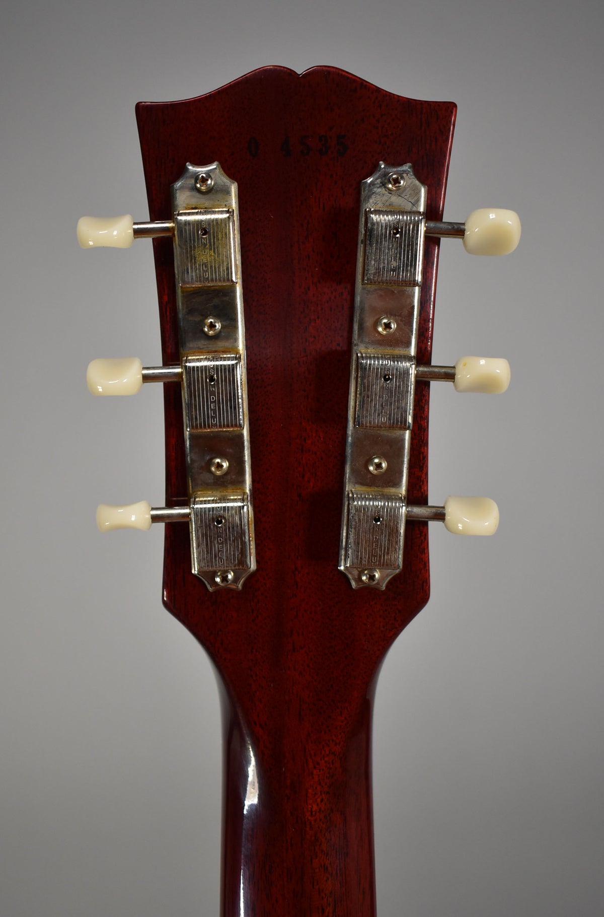 The back of a cherry red headstock and neck, showing six cream tuning pegs and two rows of three nickel tuners.