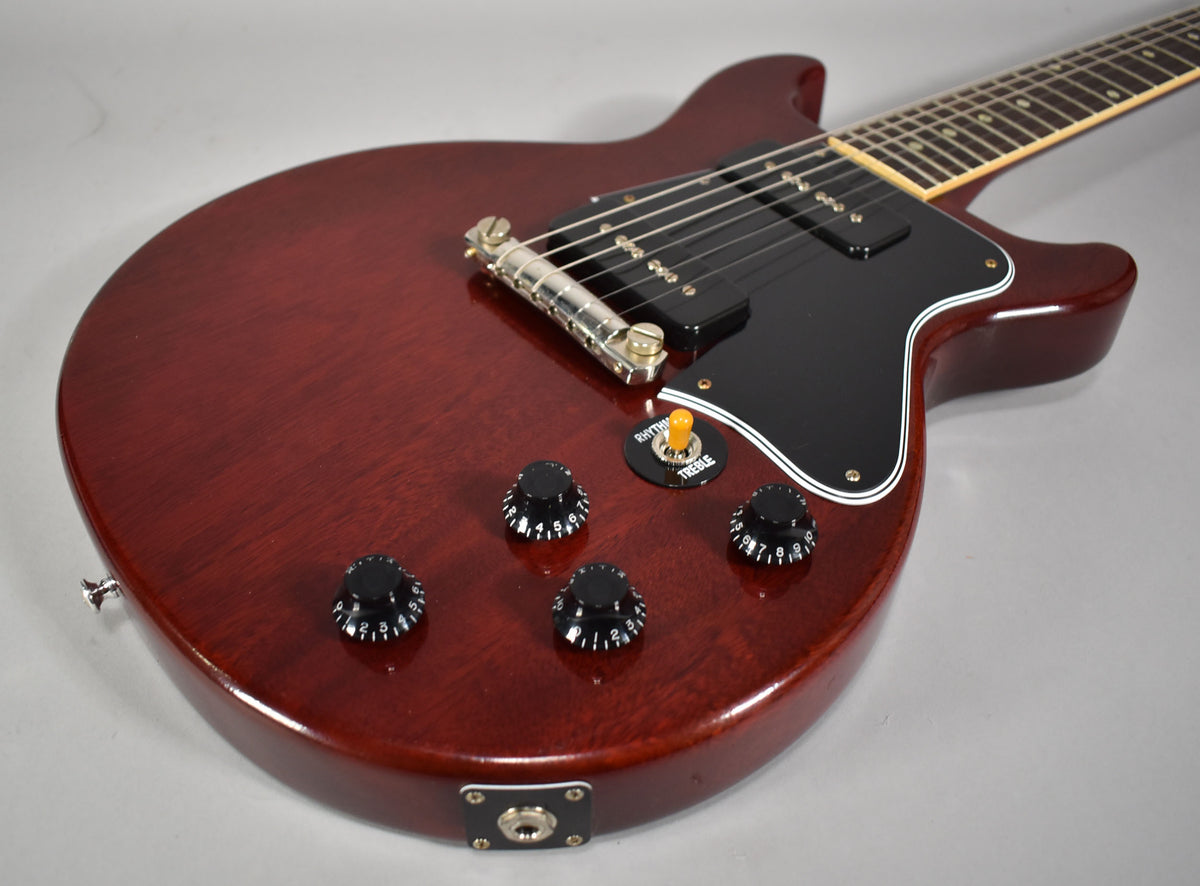 Cherry red double cutaway electric guitar, angled from the lower bout, showing four black numbered control knobs and a yellow-tipped toggle switch.