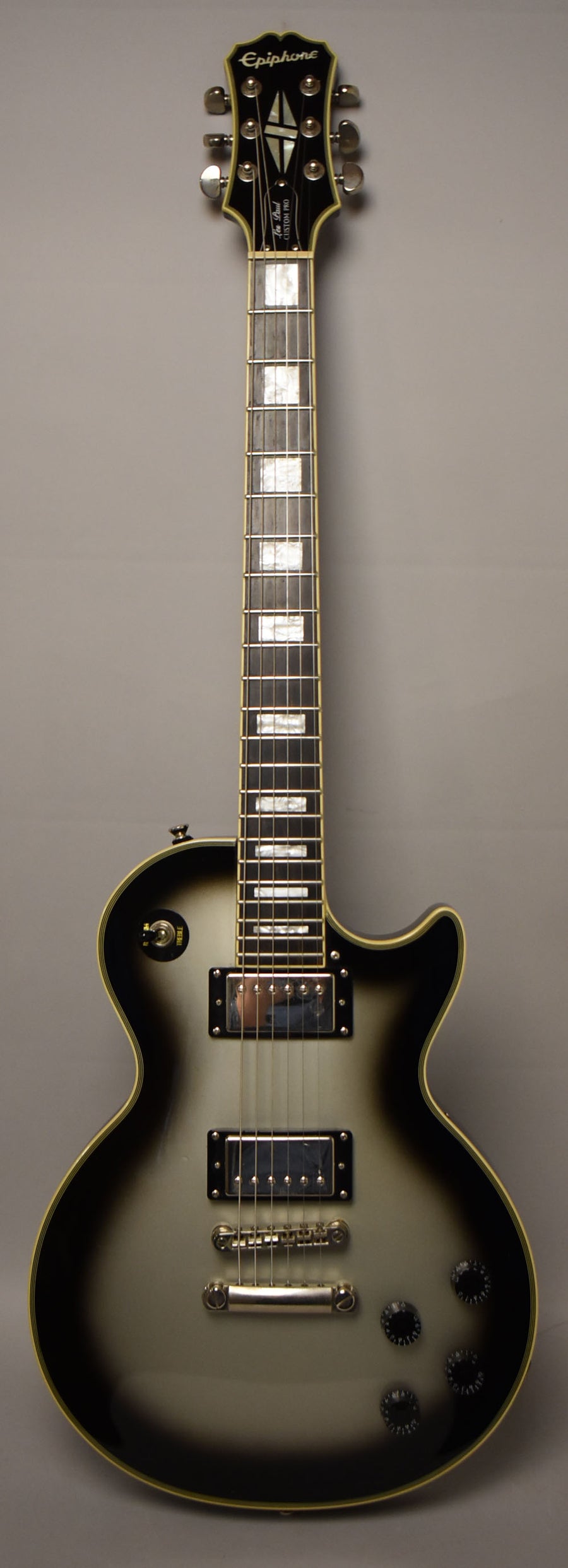 Full-front view of a silverburst electric guitar with cream binding, chrome hardware, black pickup rings, and trapezoid fretboard inlays.
