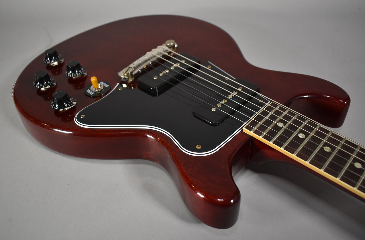 Cherry red double-cut guitar body, angled from upper left, showing black pickguard, four black knobs, amber switch, and two black P90 pickups.