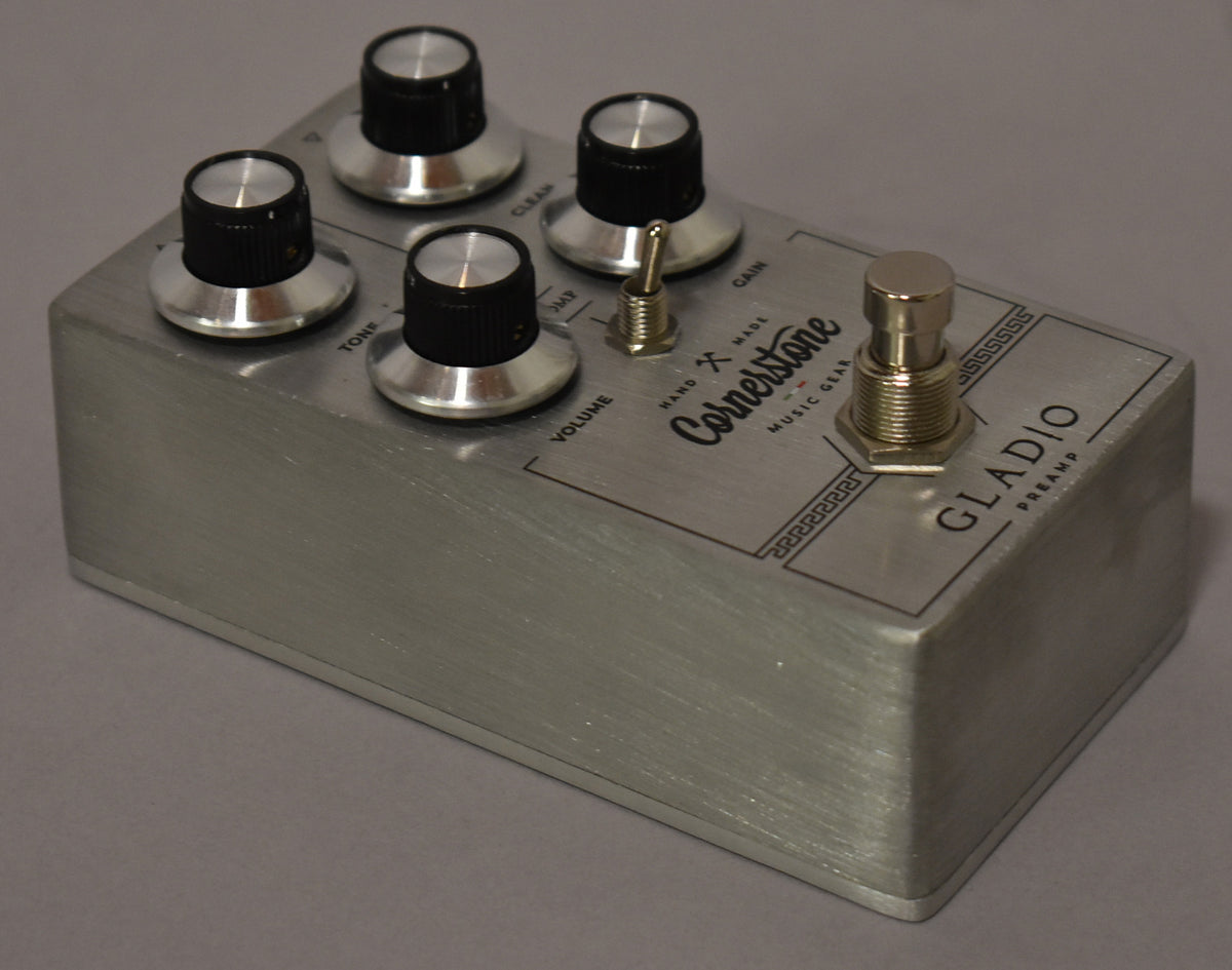 Brushed silver pedal, angled from above, showing five black and silver knobs, a small toggle switch, and a large footswitch.