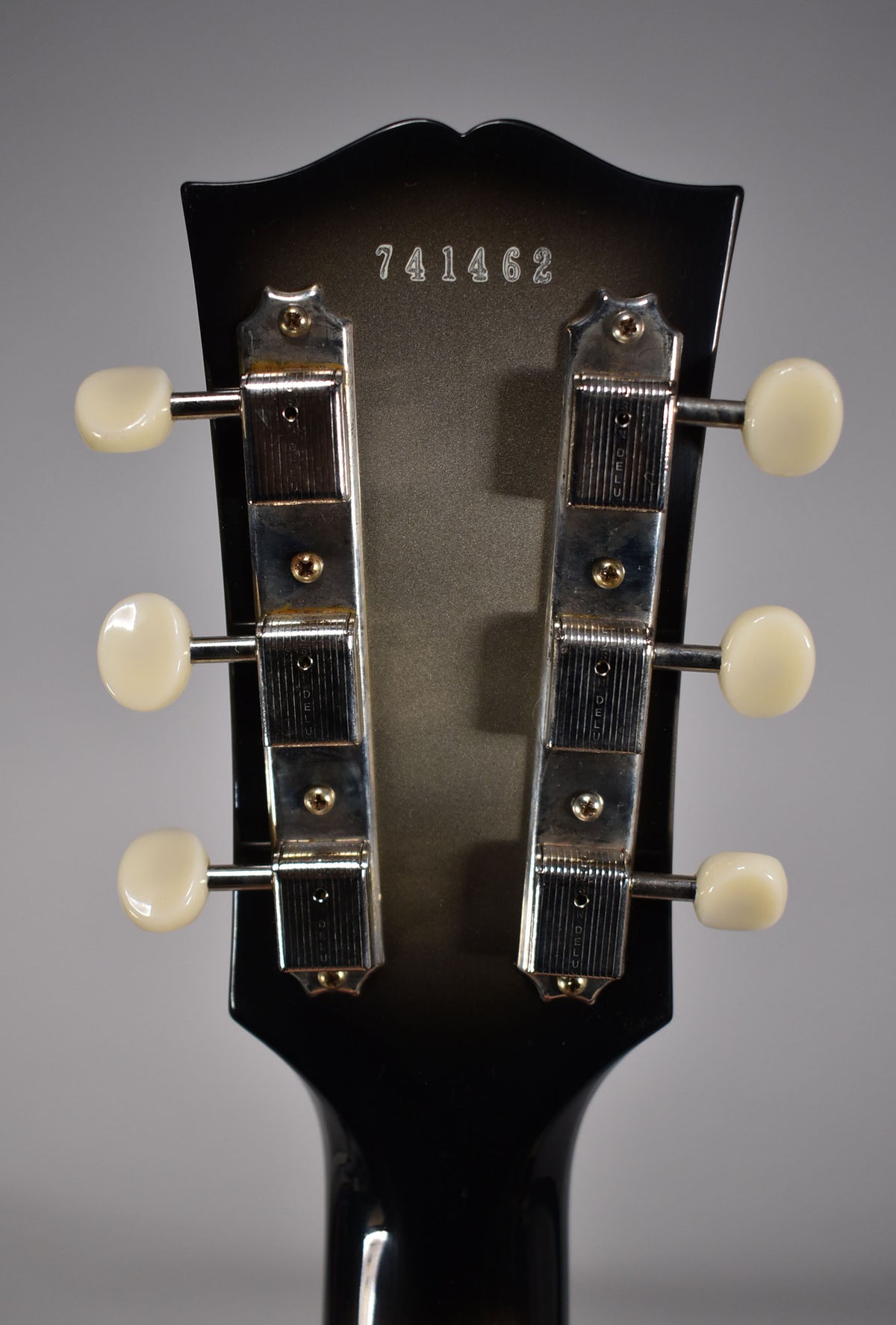 The guitar's headstock back, showing a silverburst finish, six cream tuner buttons, and chrome tuning machines.