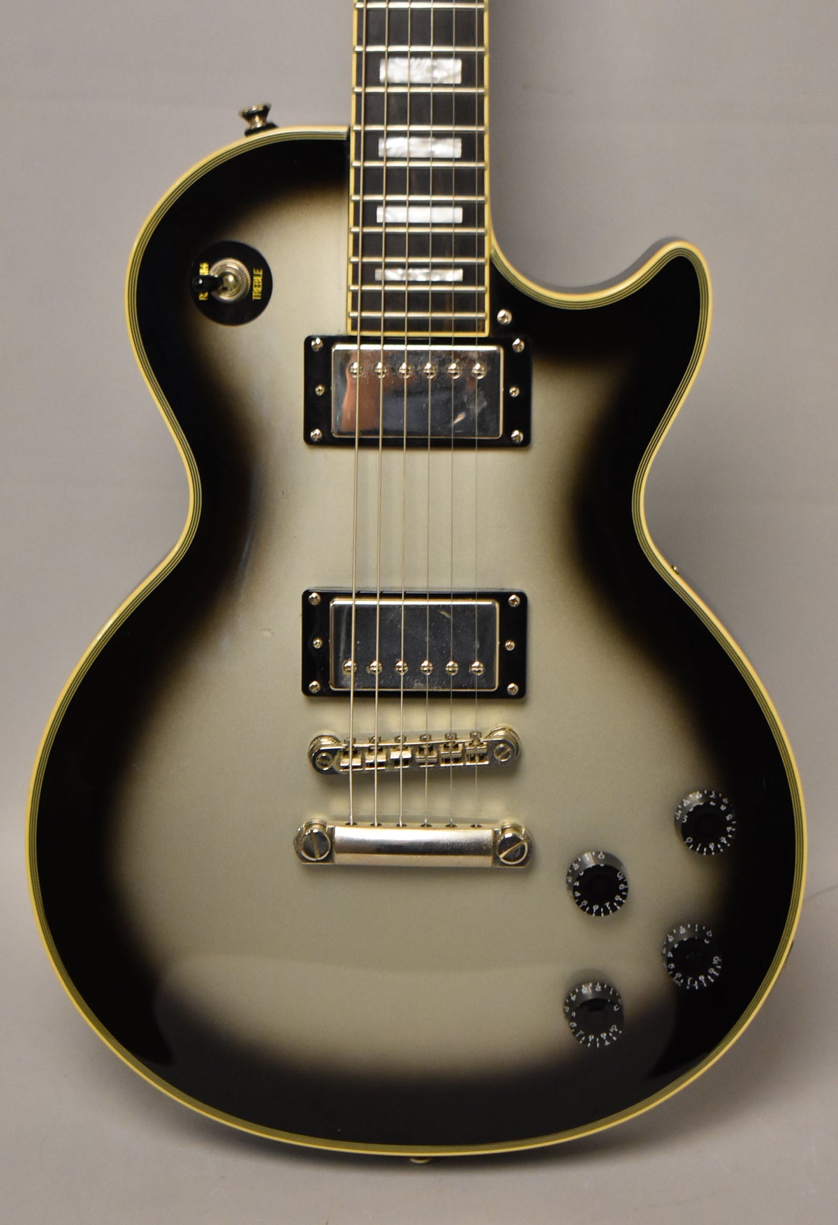 Full-frame view of a silverburst Les Paul-style guitar with chrome hardware, two humbuckers, and four black control knobs.
