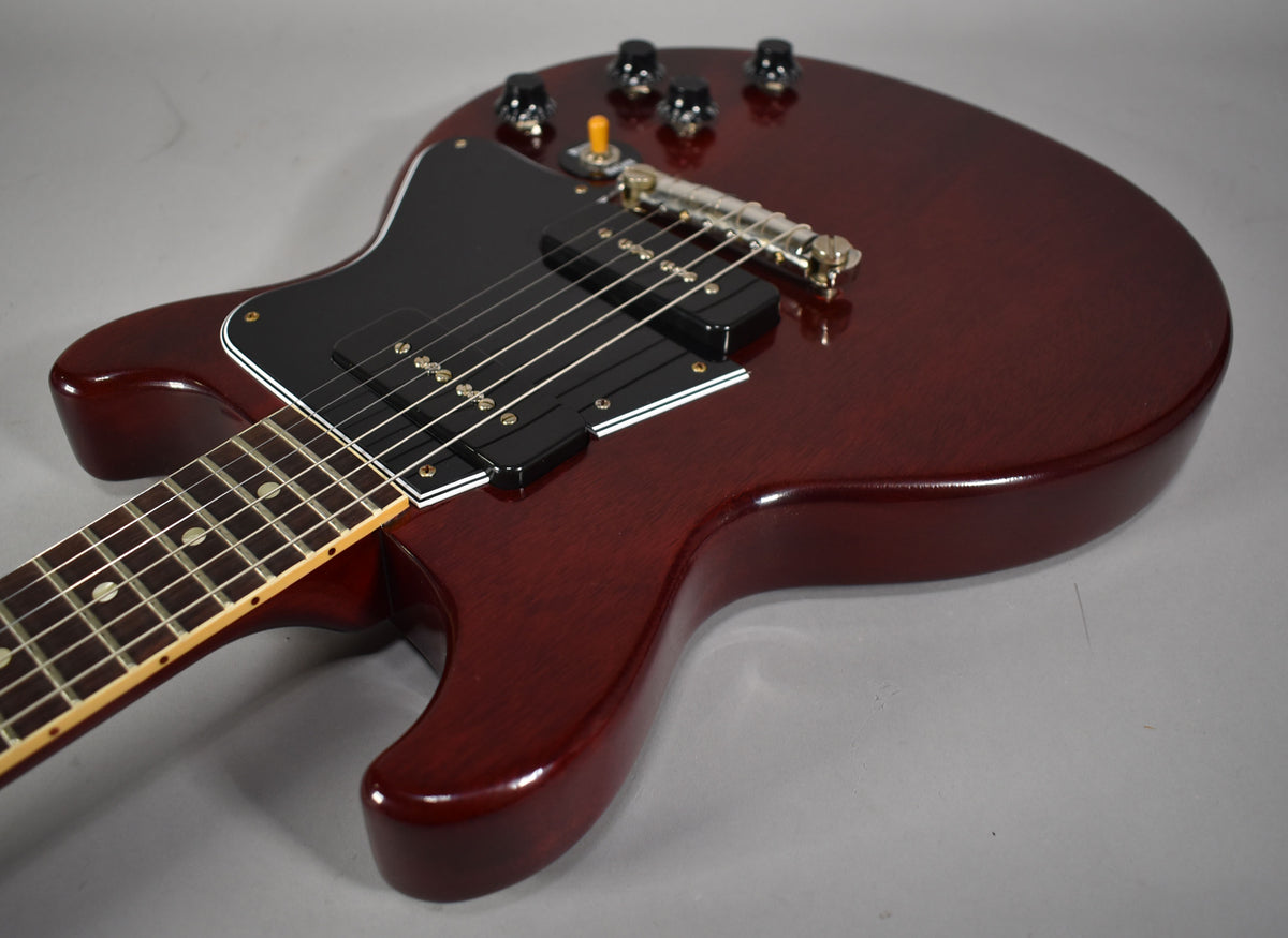 The cherry red double-cutaway body is angled from the lower bout, showing the black pickguard, two P90 pickups, and four black control knobs.