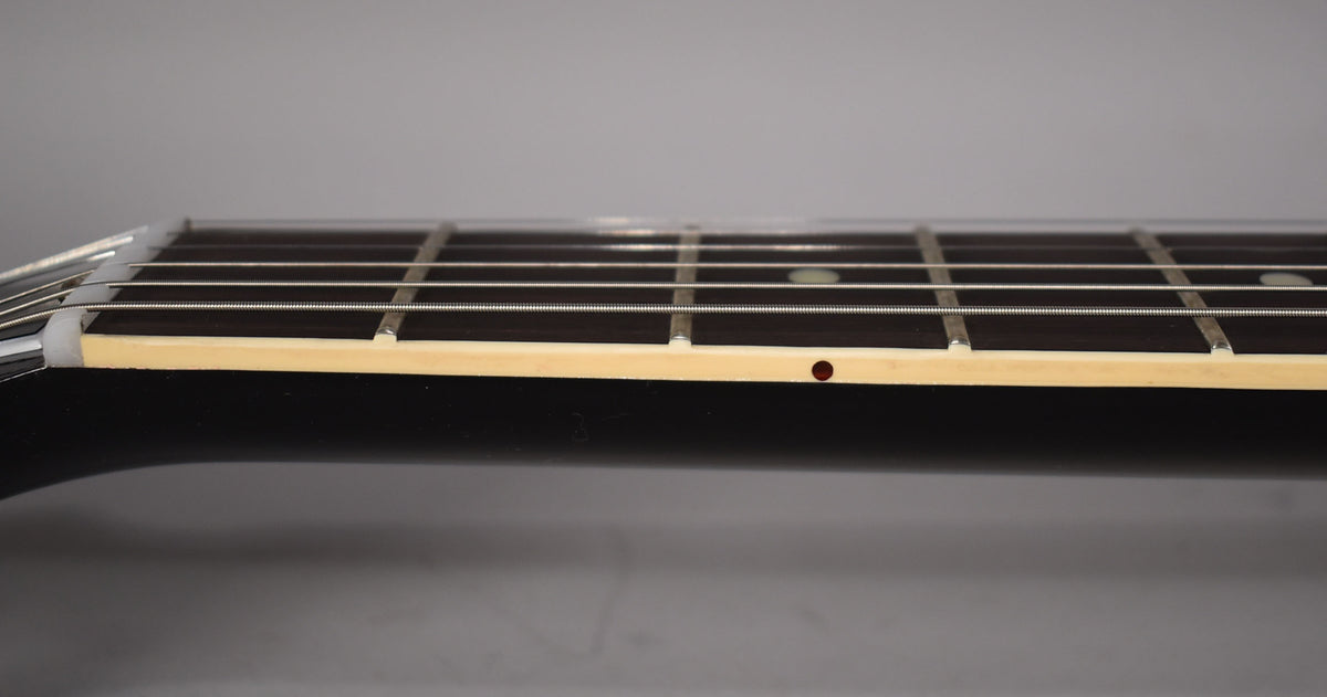 Close-up of the guitar's dark fretboard and light binding, showing the nut, frets, strings, and a single red side dot marker.