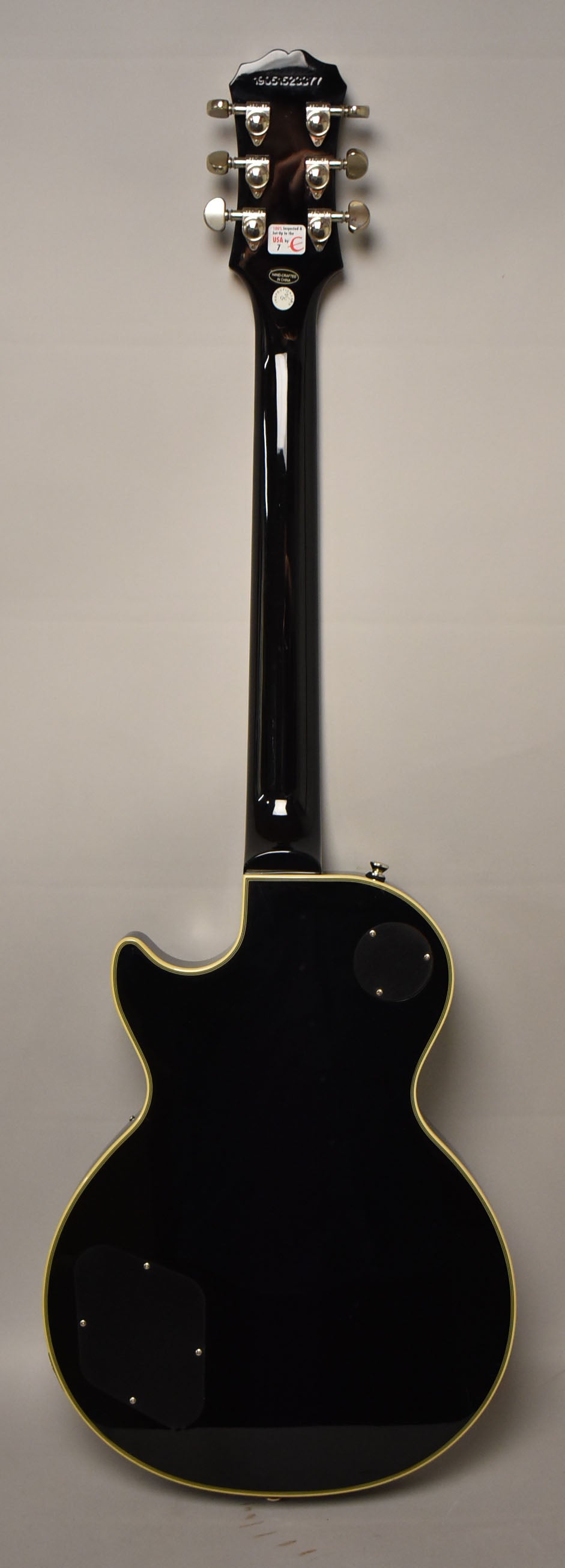 Full rear view of a black gloss guitar with cream binding, showing the headstock with six chrome tuners and two control cavity covers.