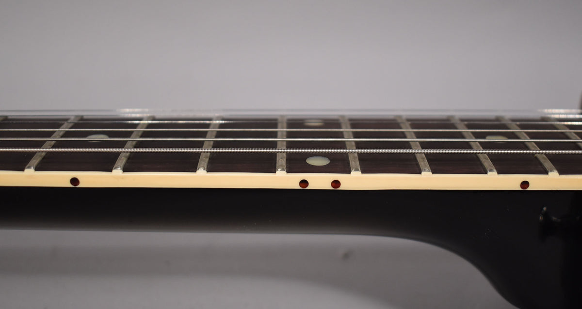 Close-up of the guitar's dark fretboard with white binding, showing frets, white dot inlays, and small red side dots.