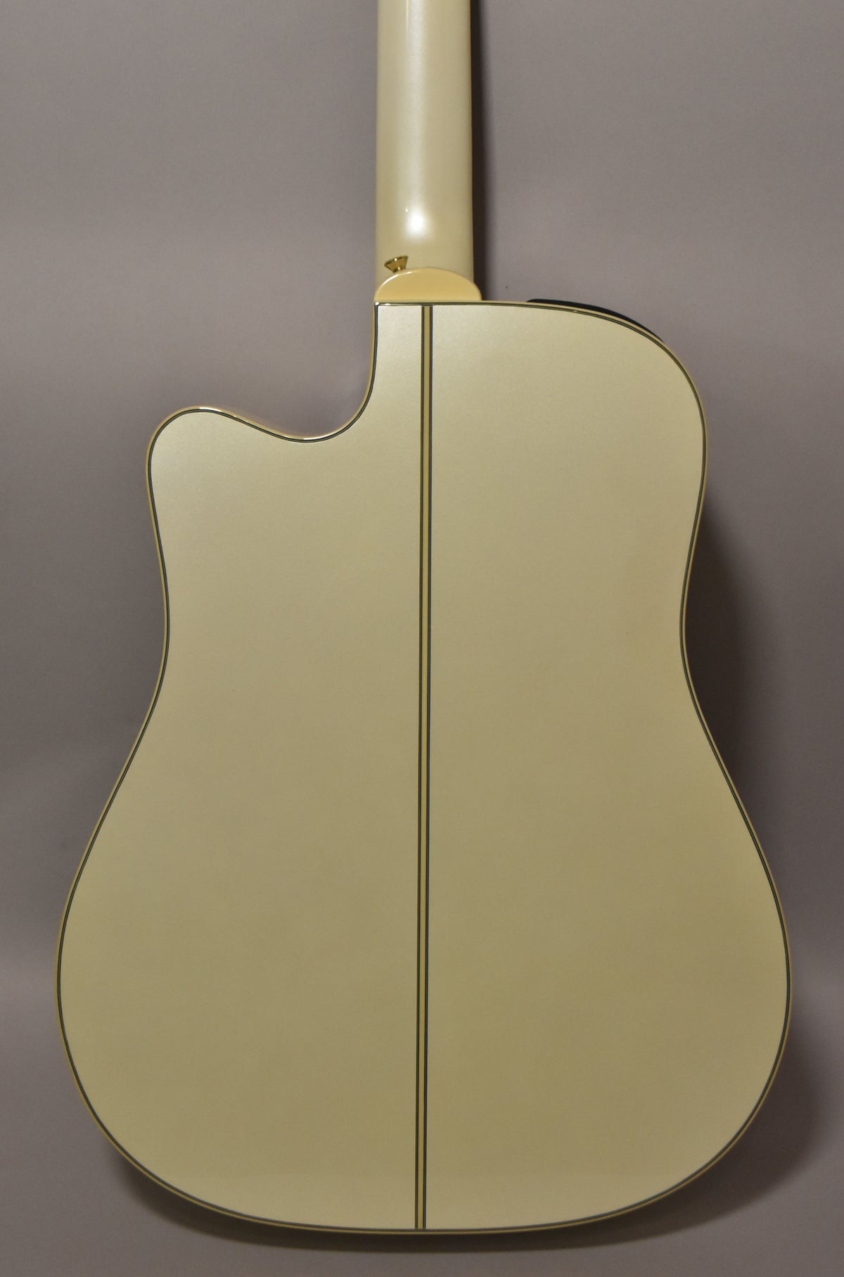 The back of a pearl white dreadnought acoustic-electric guitar, showing the cutaway, neck heel, and a dark center strip.