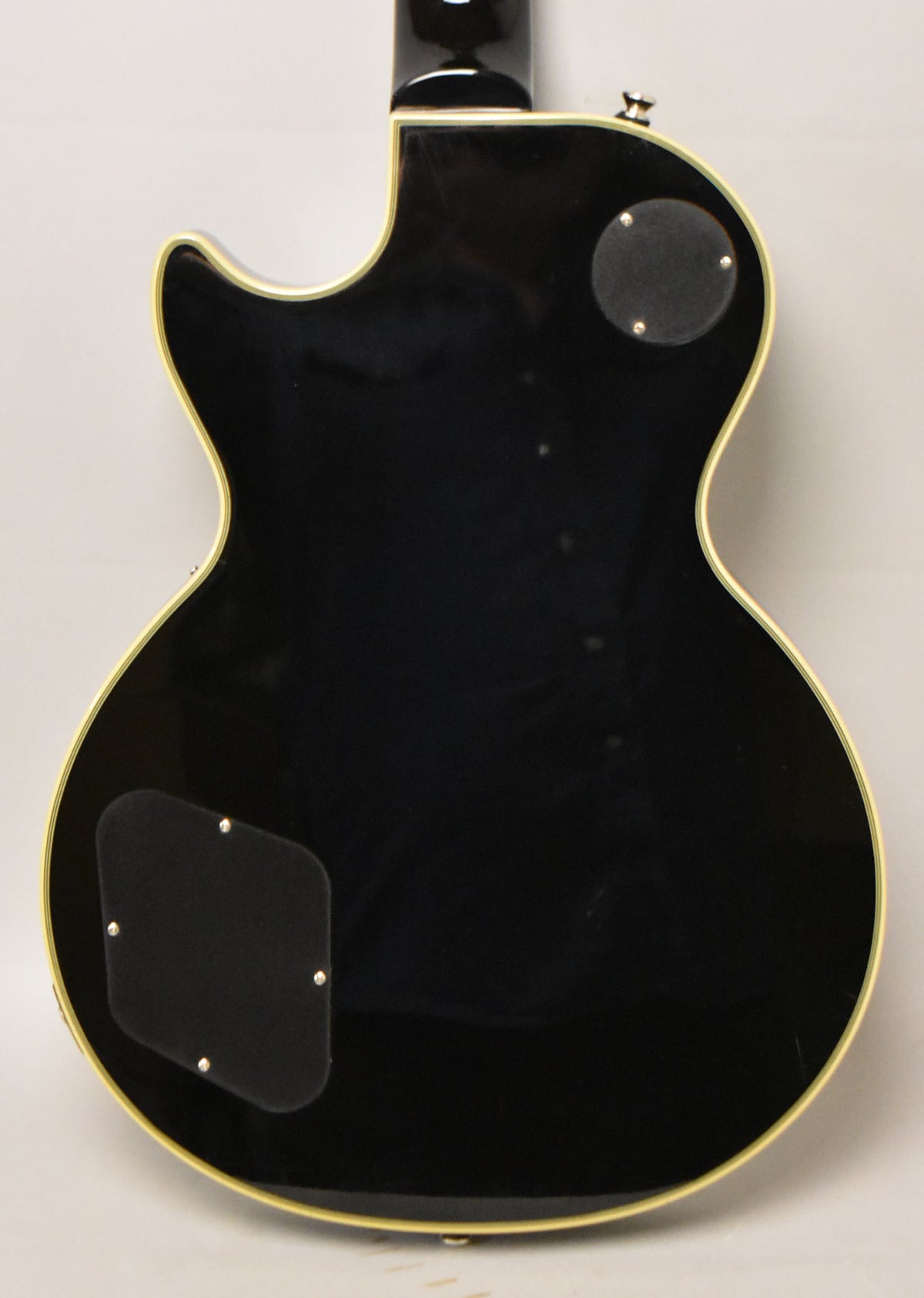 The guitar's glossy black back, with cream binding, shows two black control cavity covers and light surface scratches.