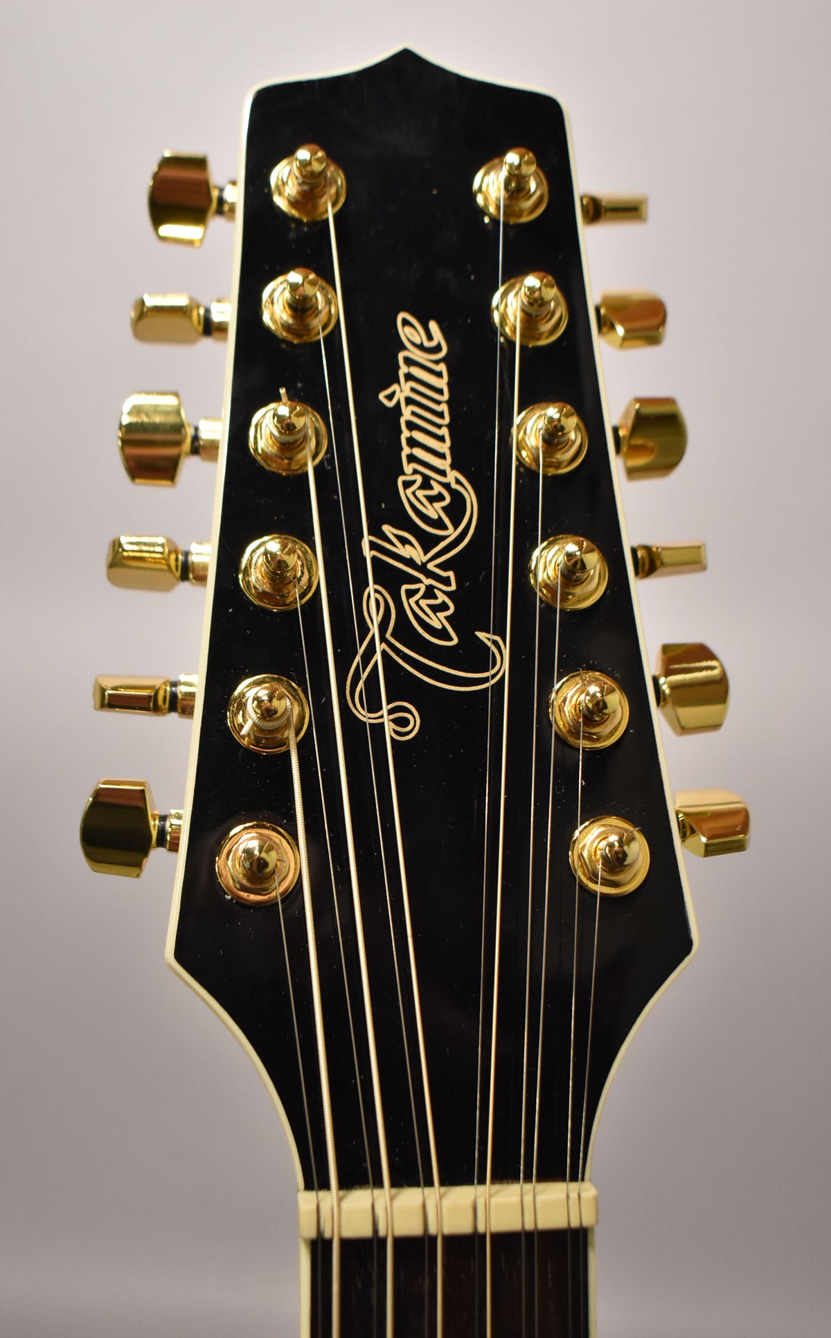 Close-up of the guitar's black headstock with a white binding, showing 12 gold tuning pegs and strings, with light wear.