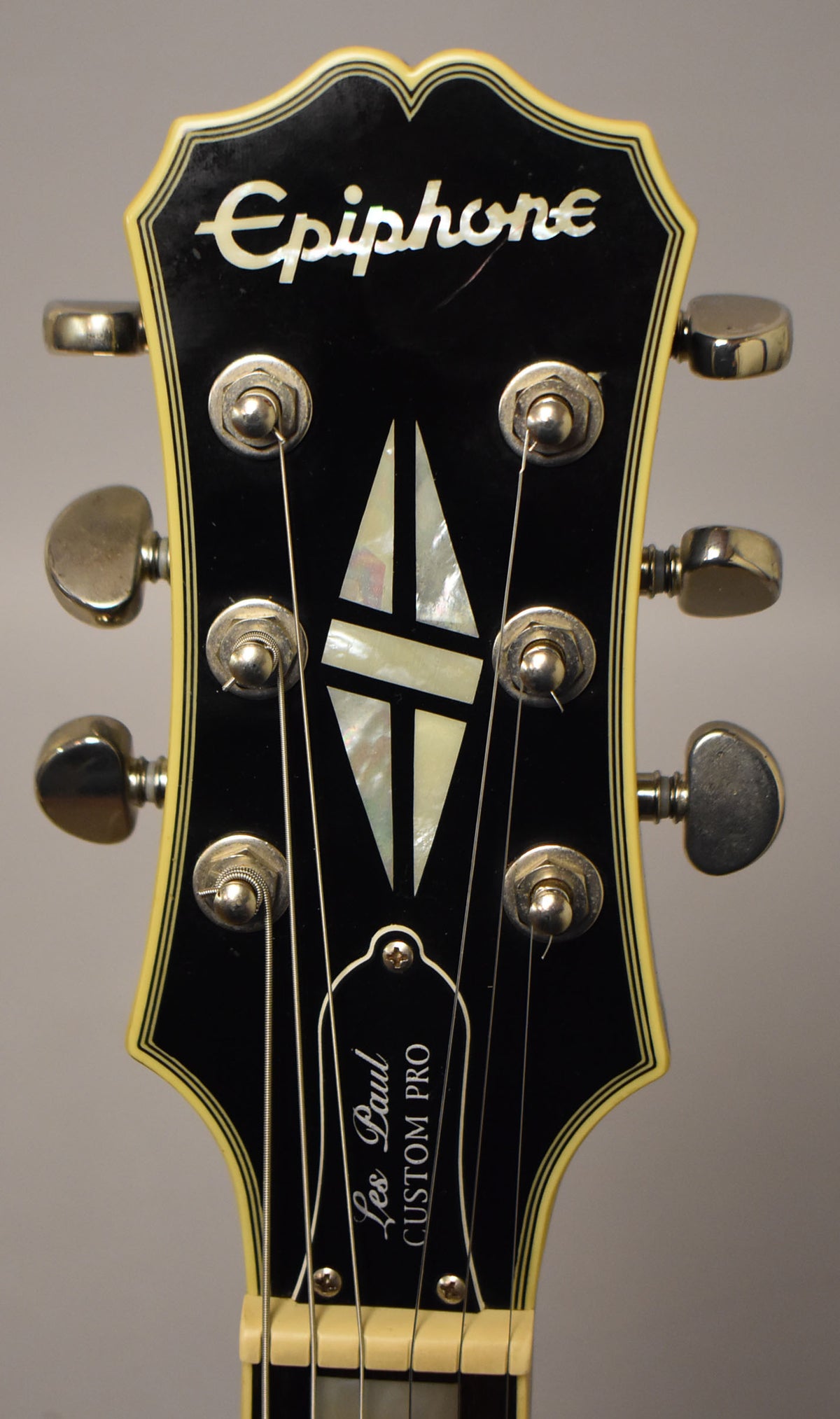 Close-up of the black headstock with cream binding, showing six chrome tuners, mother-of-pearl inlay, and a few light scratches.