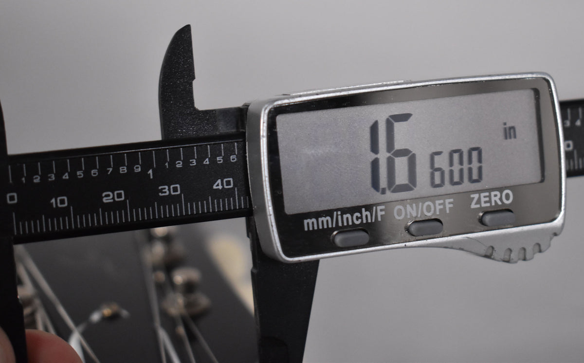 A digital caliper measures the nut width of the guitar at 1.600 inches, with the headstock and strings visible below.
