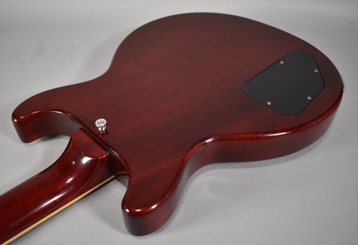 The guitar's cherry red back, with a visible wood grain, features a black control cavity cover and a chrome strap button.
