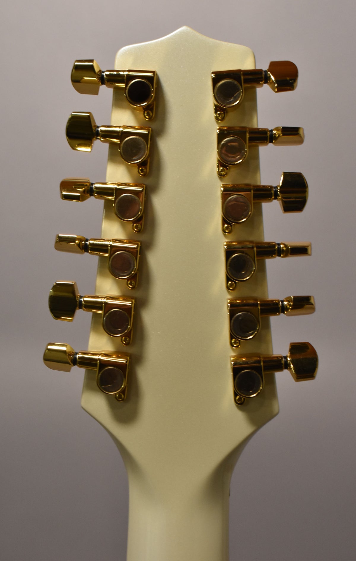 The back of a pearl white 12-string guitar headstock with 12 gold tuning machines, 6 on each side.
