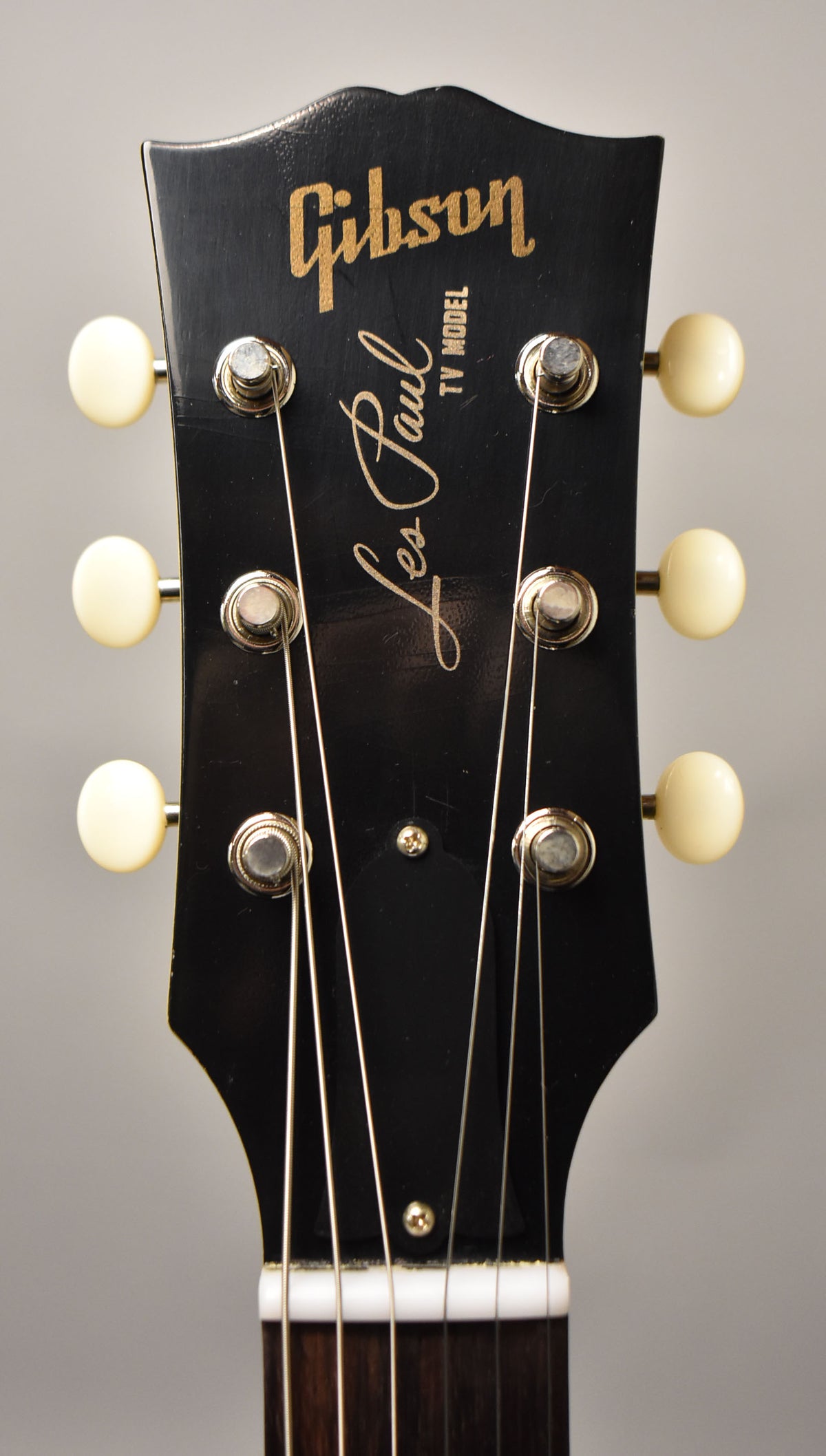 Full-frame view of the black headstock with six cream tuning pegs, showing light wear and checking on the finish.