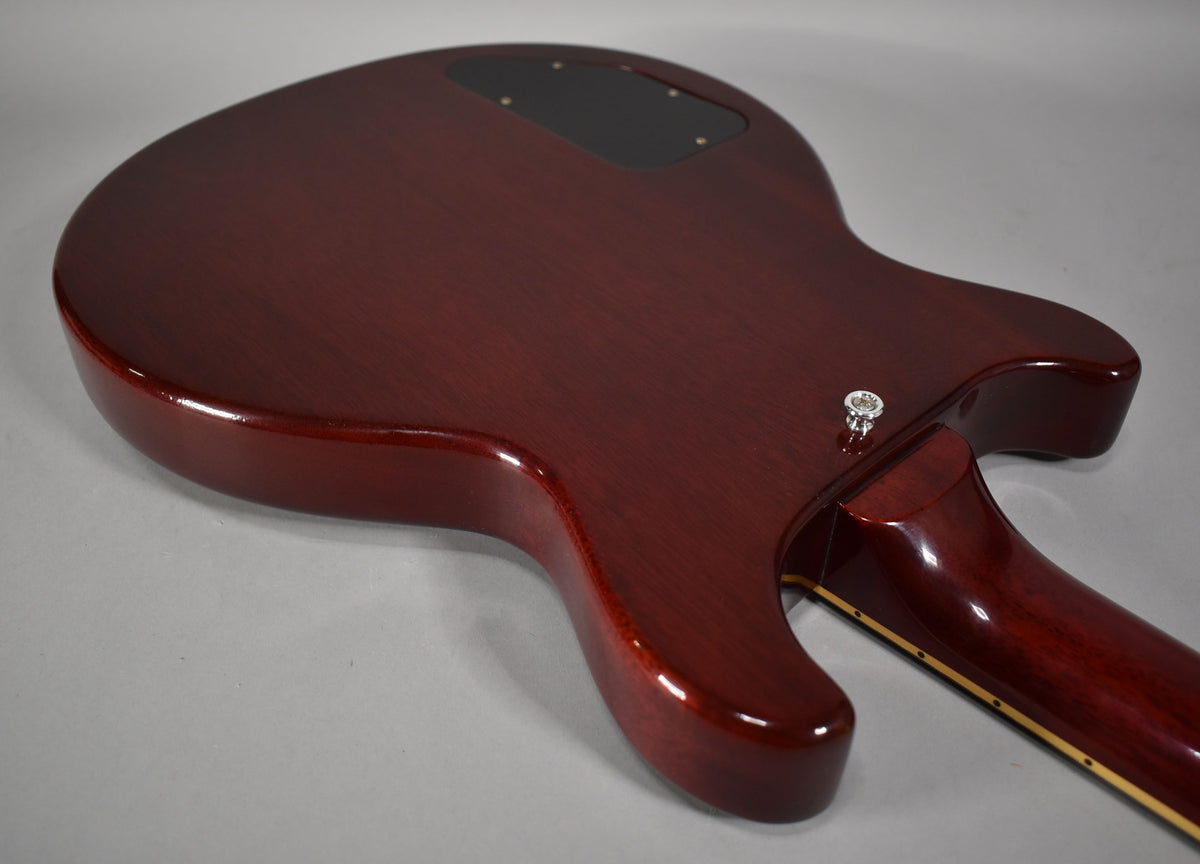 The guitar's cherry red body and neck are viewed from the back, showing a black control cavity cover and strap button.