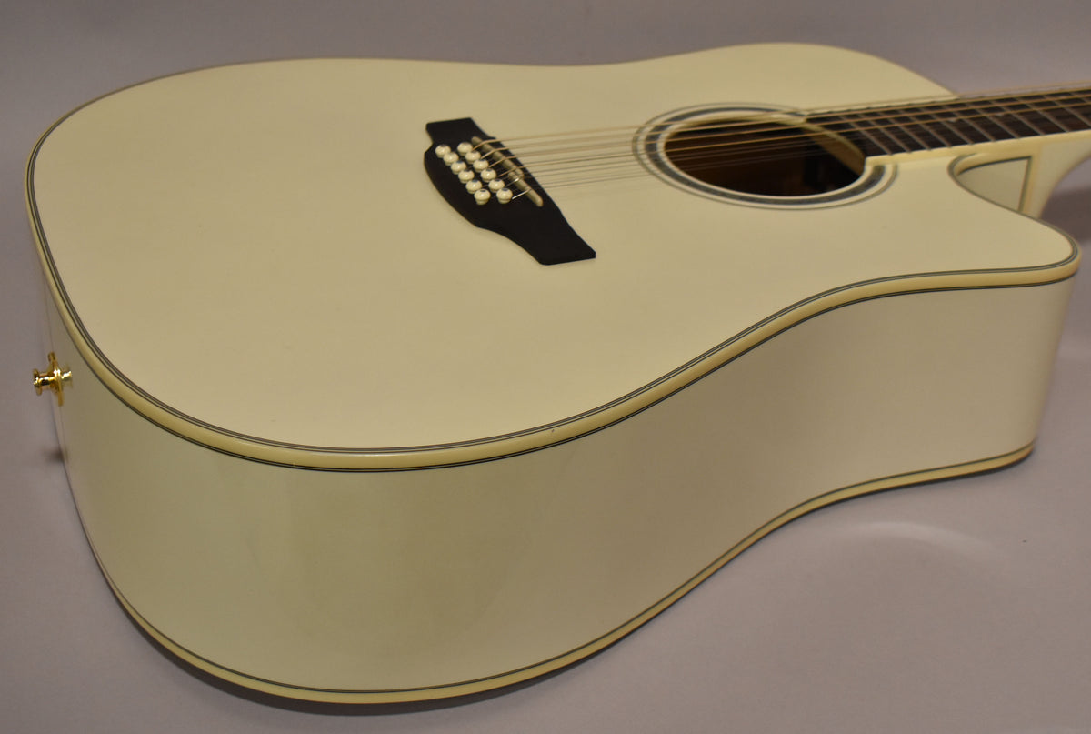 The pearl white 12-string acoustic-electric guitar is angled from the lower bout, showing the cutaway and gold endpin jack.