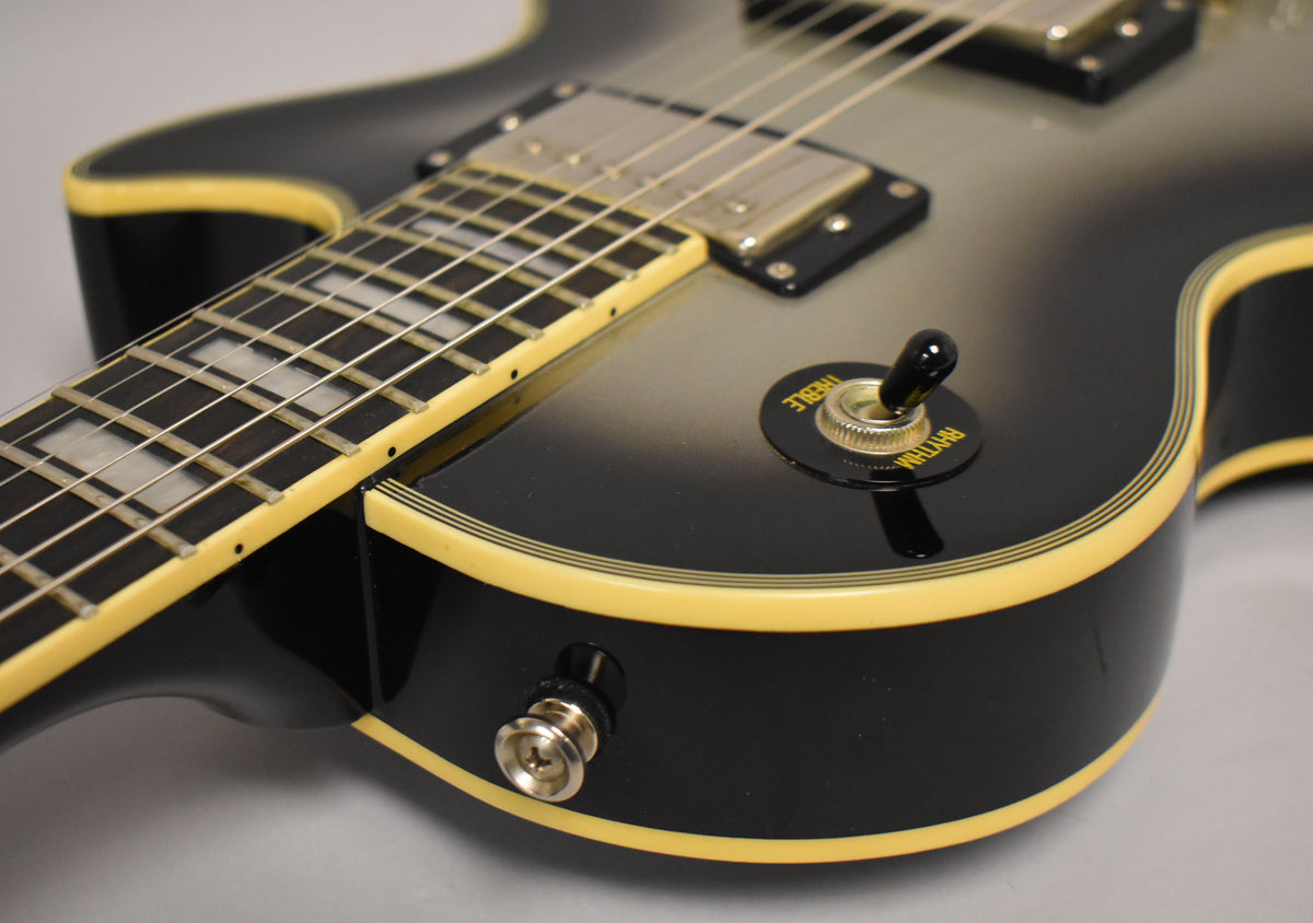 The silverburst guitar's body and neck are visible, with cream binding, chrome hardware, and a black pickup selector switch.