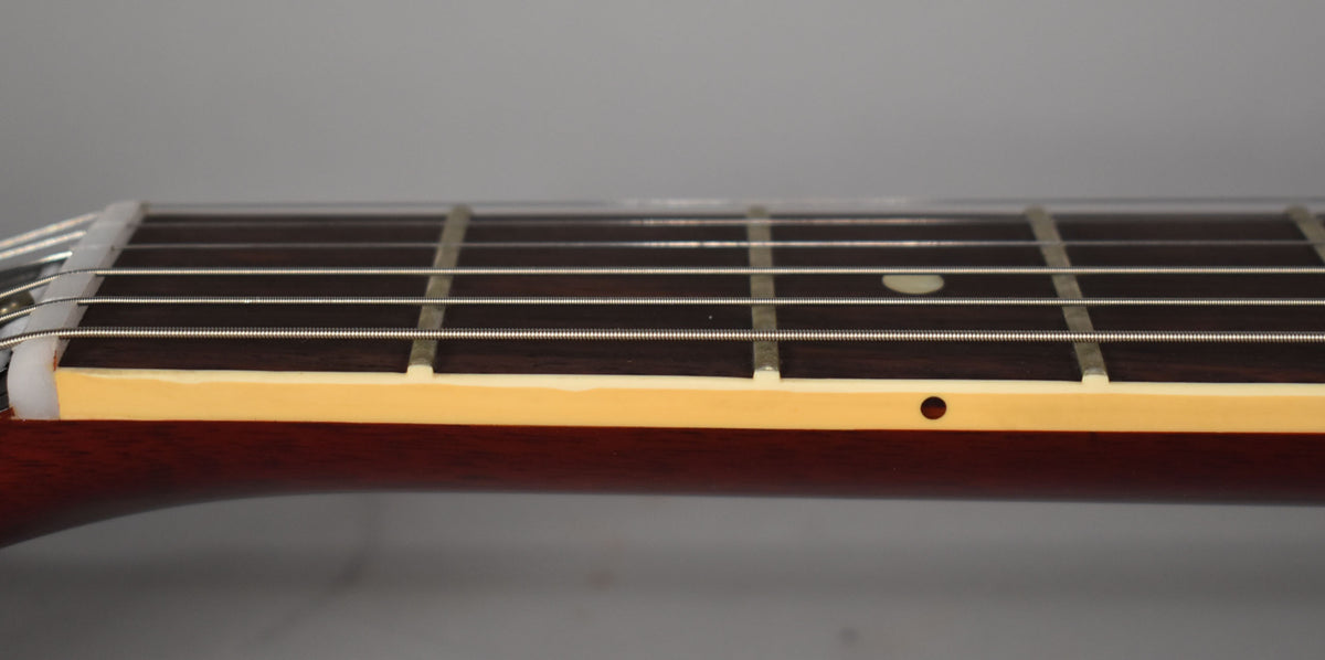 Close-up of the guitar's dark fretboard, showing metal frets, white string nut, cream binding, and a single dot inlay.