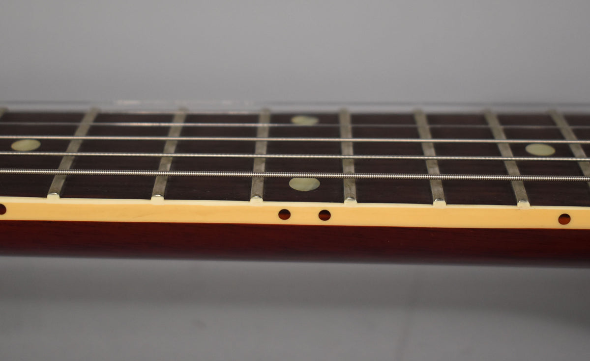 Close-up of the guitar's dark fretboard with cream binding, showing frets, strings, and light circular inlays.